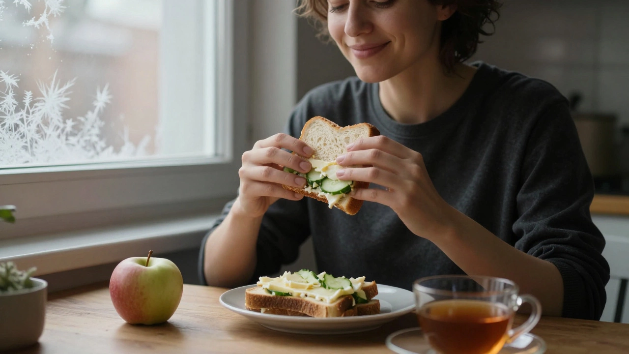 Человек спокойно ест бутерброд с сыром и огурцом, рядом чашка чая и яблоко.